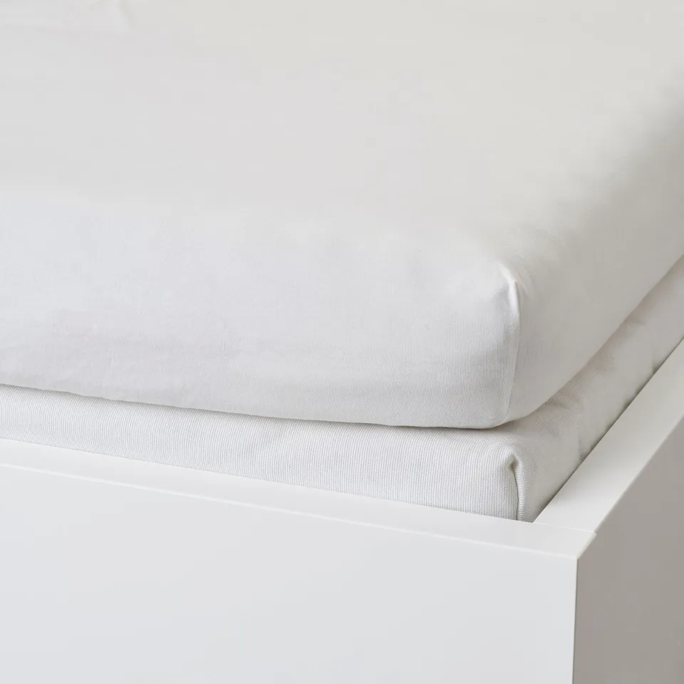 A white cotton jersey bed sheet displayed on a white platform, showcasing its fitted design with elastic edges.
