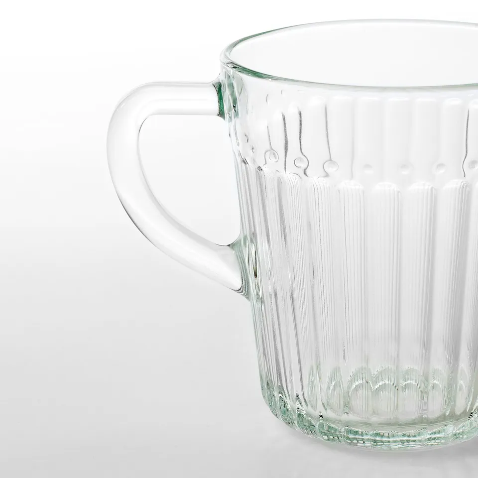 Clear glass mug with a sturdy handle, showcasing vertical ribbing for grip, standing on a plain surface.