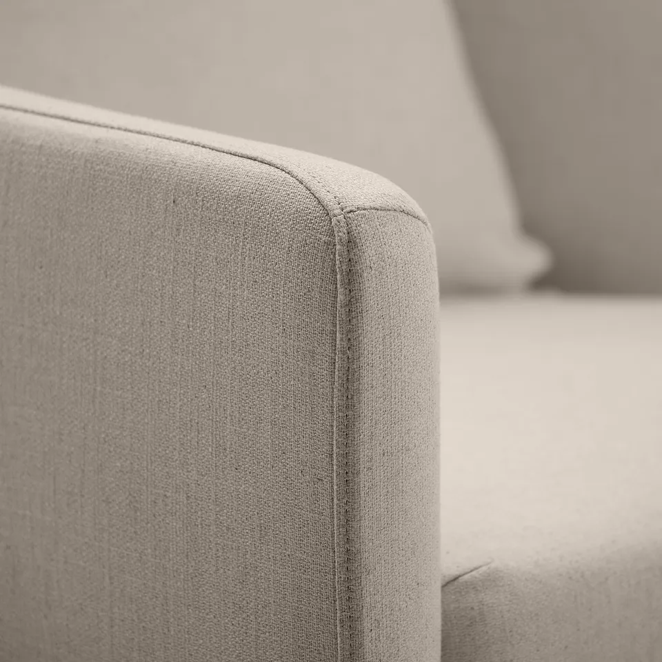 Close-up of a cosy, upholstered armchair corner, showcasing soft, textured fabric and neat stitching.