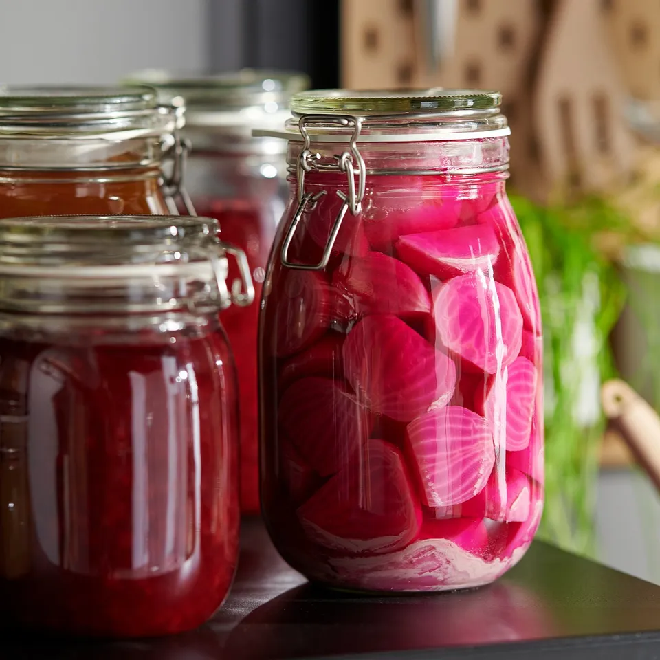 Three clear jars with metal clamps hold bright pink pickled vegetables. One jar is in the foreground, showcasing the airtight seal.