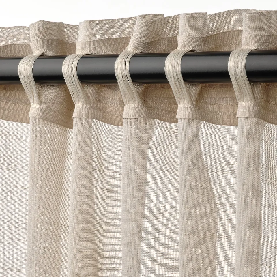 Sheer beige curtains hang with pleated tops on rod, offering light diffusion and privacy.