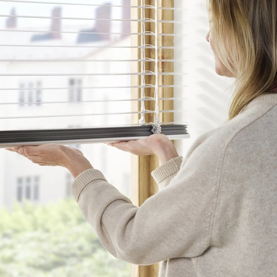 A person adjusts venetian blinds by pulling a cord, controlling light and privacy.