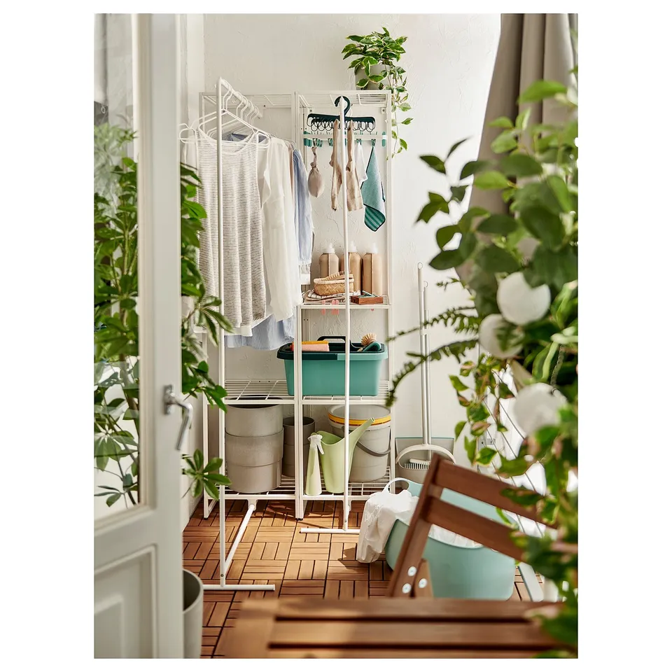 Balcony laundry station: JOSTEIN white, metal, with hanging shirts, baskets, and plants.