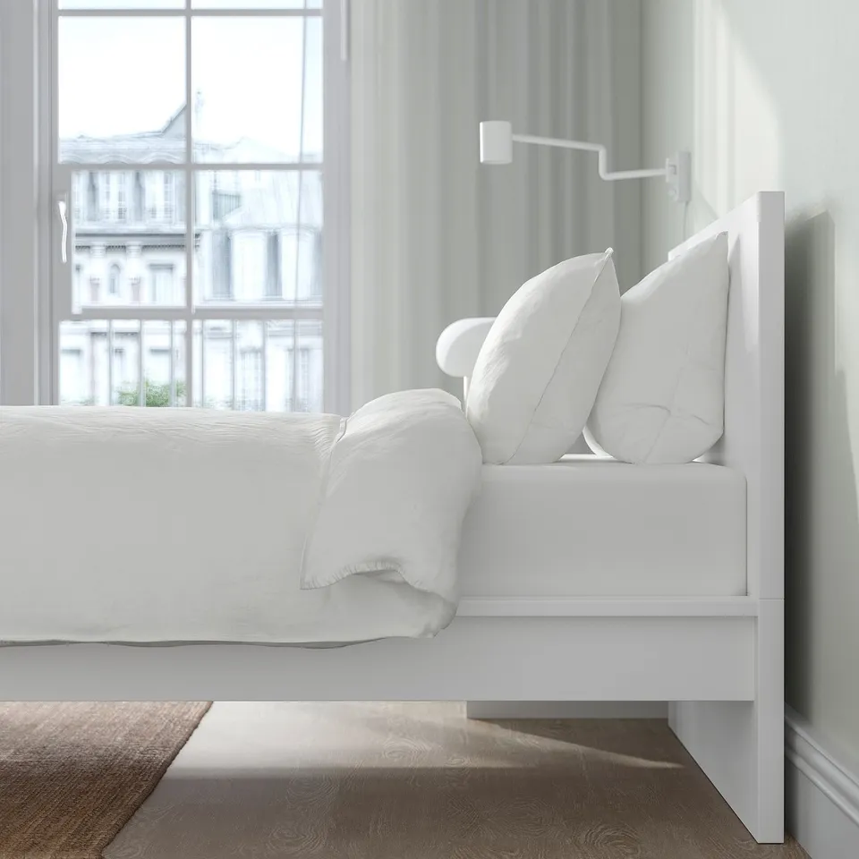 A modern, white MALM bed with a high headboard against a wall, featuring clean lines and ample pillows for comfortable seating.