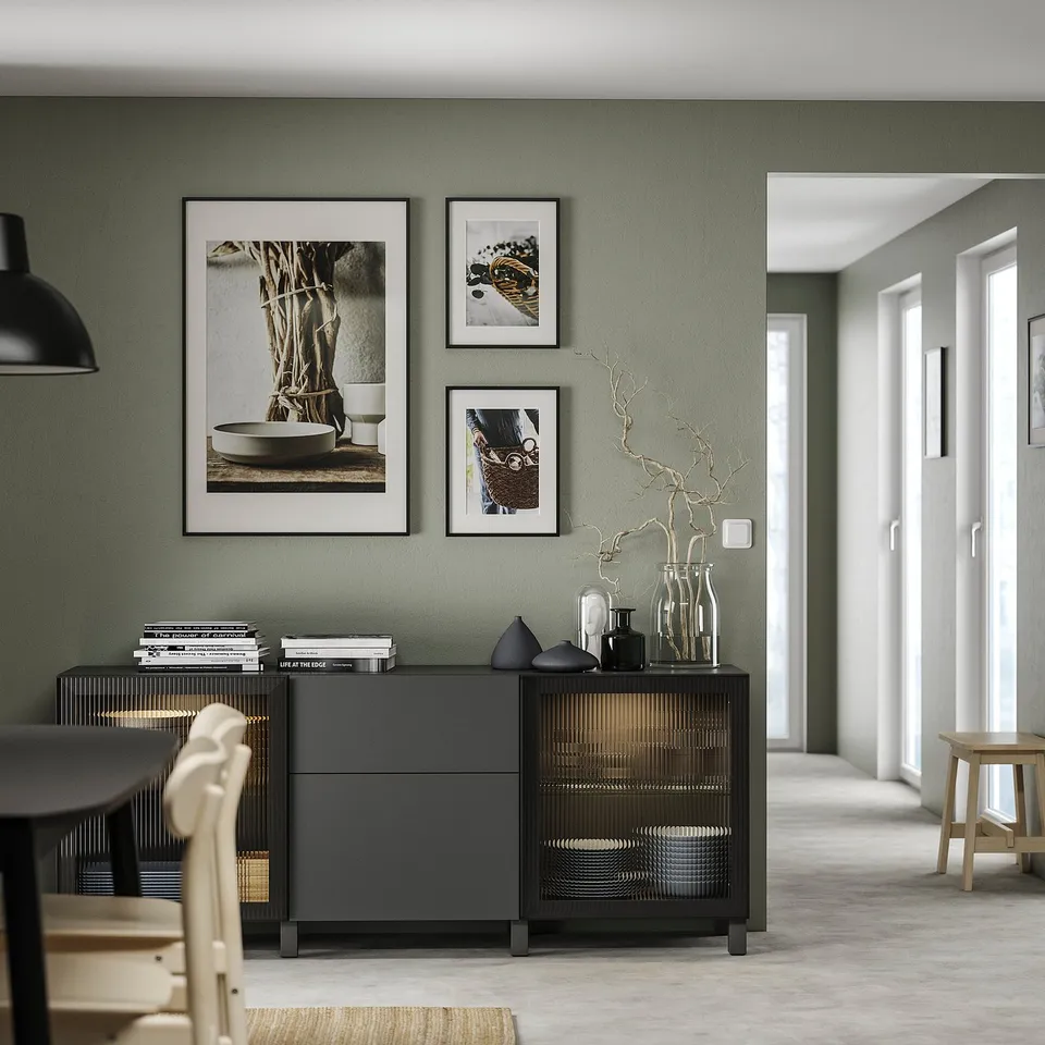 Modern living room with a green accent wall, featuring a dark grey BESTÅ storage unit with adjustable black vases and stems.