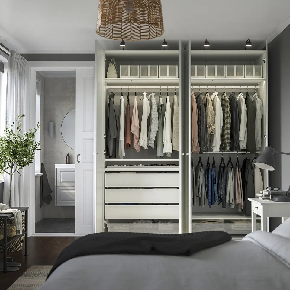 Modern bedroom with open PAX wardrobe, displaying clothing, drawers, and lit shelves.