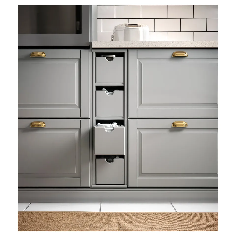 Modern grey kitchen cabinets with gold handles, including a pull-out storage box. The countertop a white appliance against a tiled backsplash.