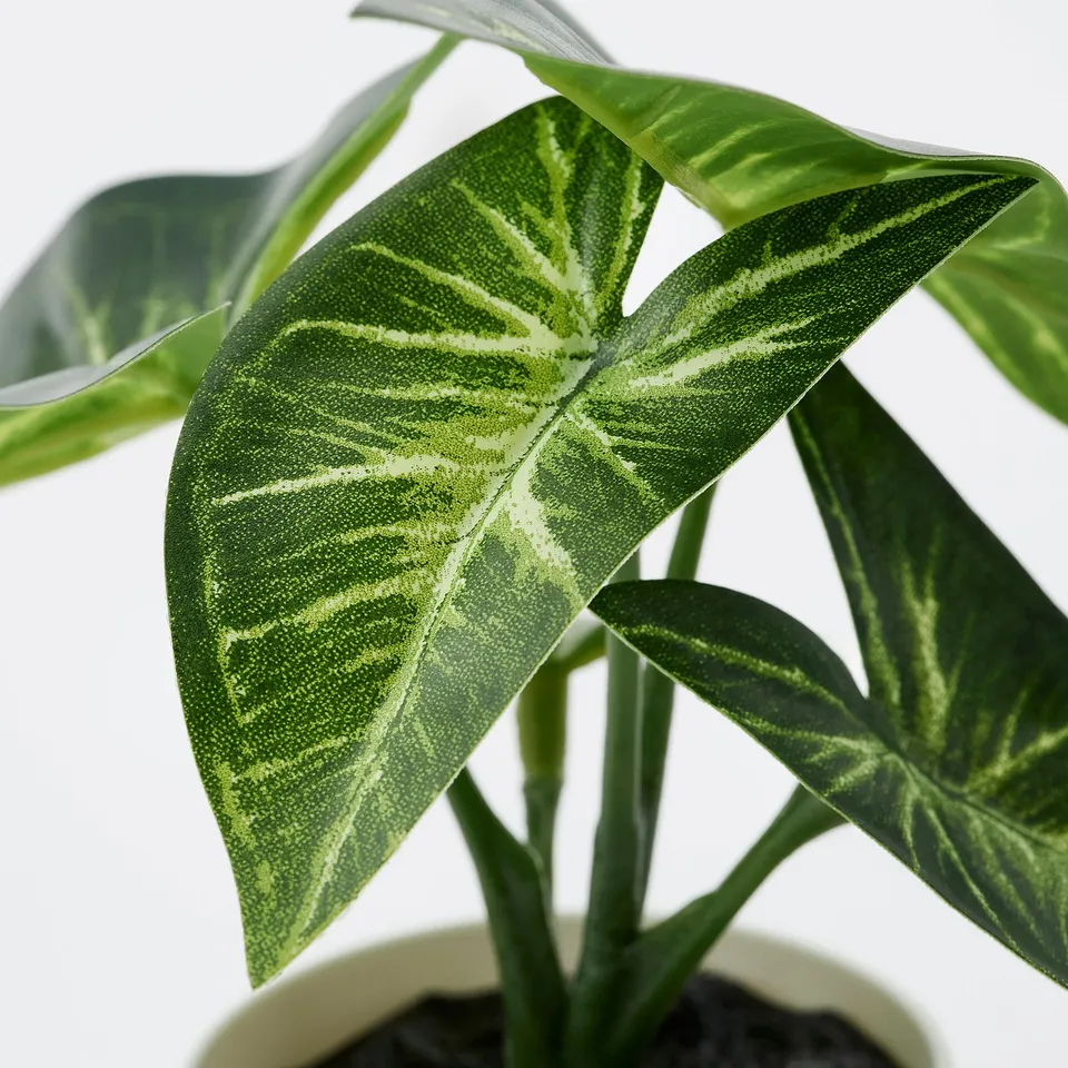 Close-up of artificial plant with vivid green, veined leaves in a white pot.