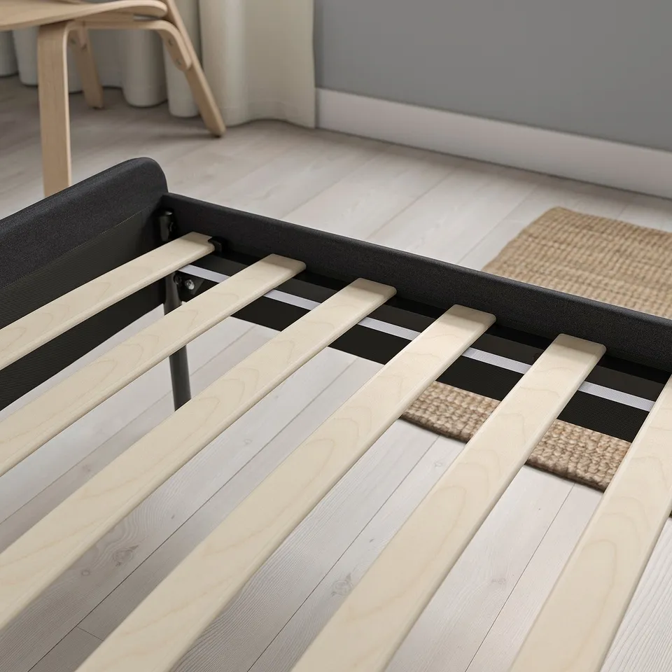 Bed frame with slats; easy to clean and assemble. Headboard softly padded. Natural wood floor and rug.