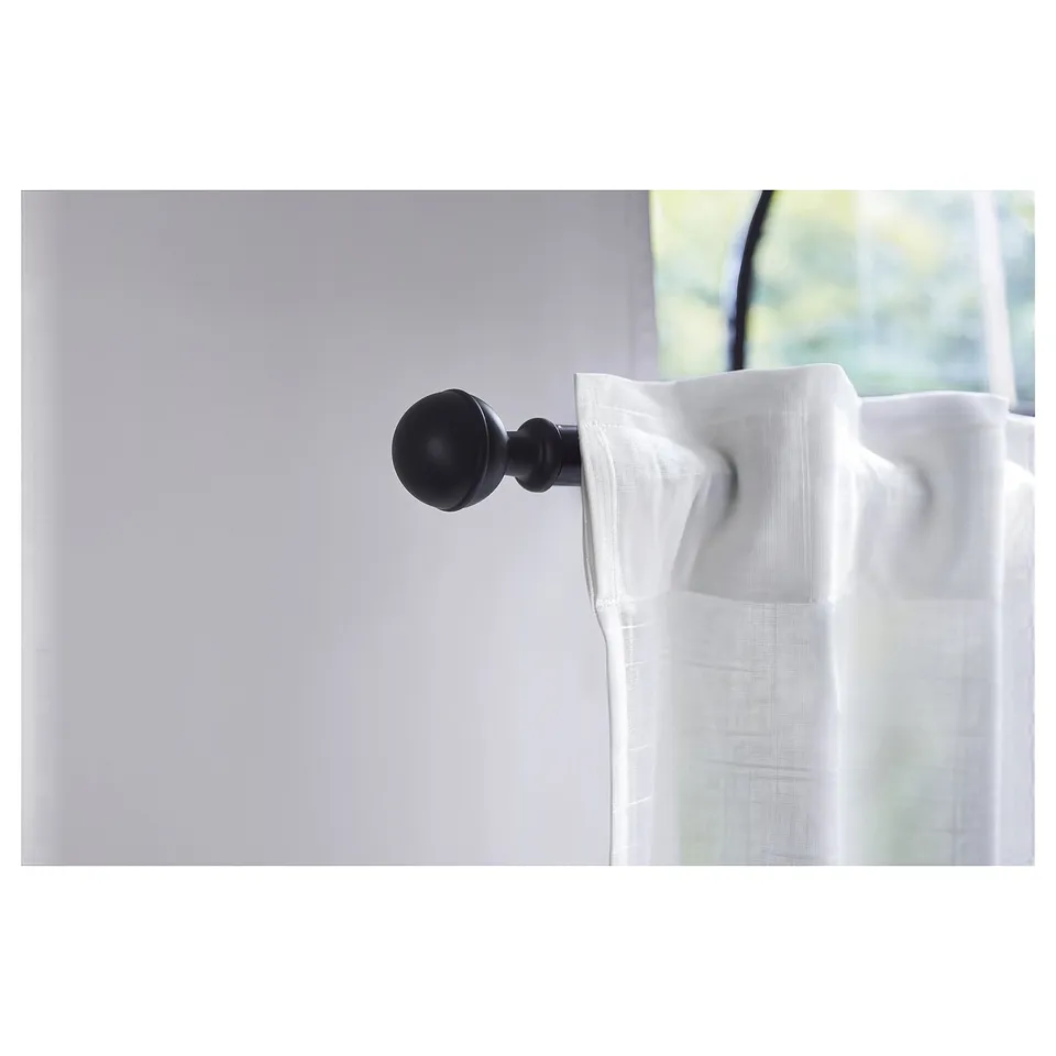 Black decorative finial on white curtain rod near a window.