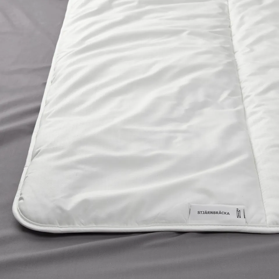 A close-up of a plush white duvet on a grey bedsheet, showing its soft, fluffy texture and branded label on the corner.
