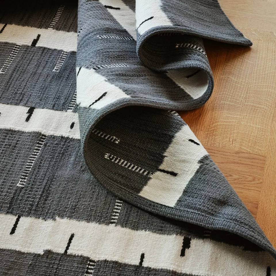 Grey handwoven wool rug with birch tree pattern on light wood floor, reversible and high quality.