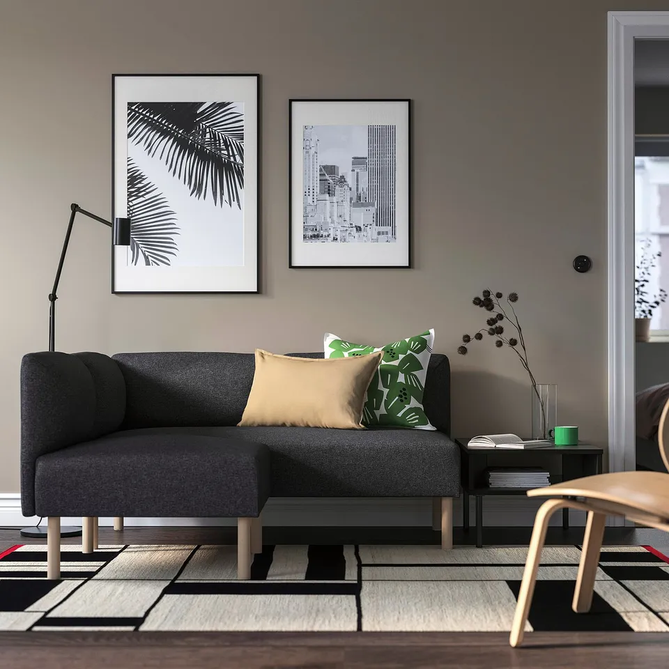 Modern minimalist living room with grey sofa, colourful cushions, wall art, side table with dried flowers, and geometric rug.