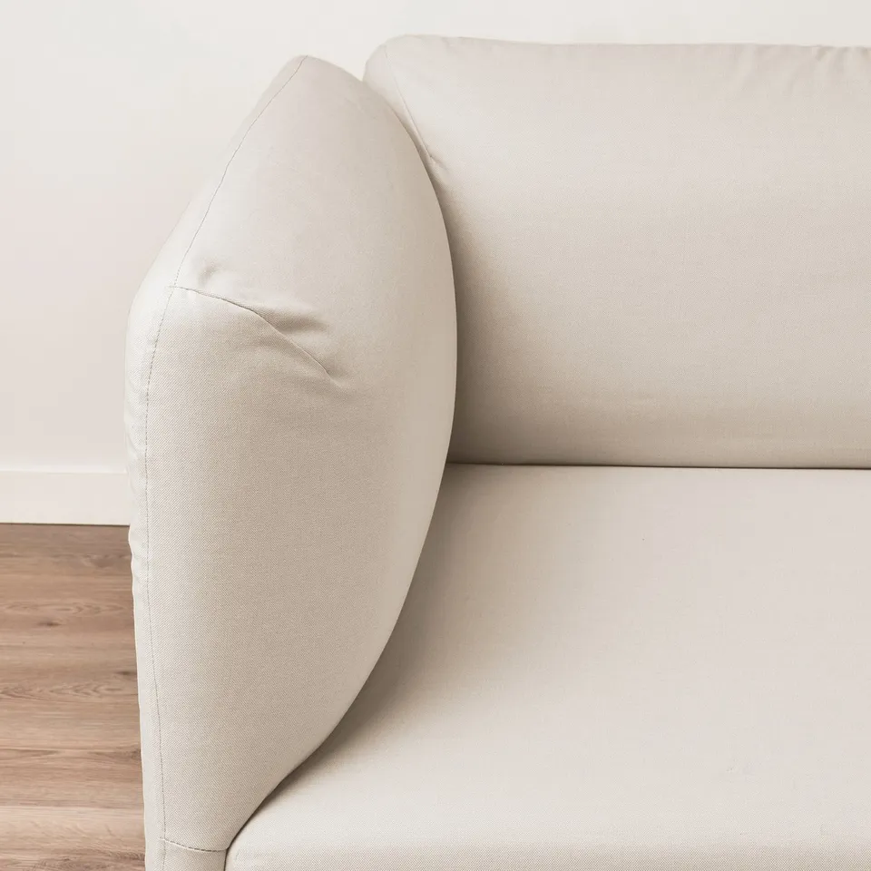 Modern sofa with smooth, beige cover; elegant, curved armrest; clean lines.