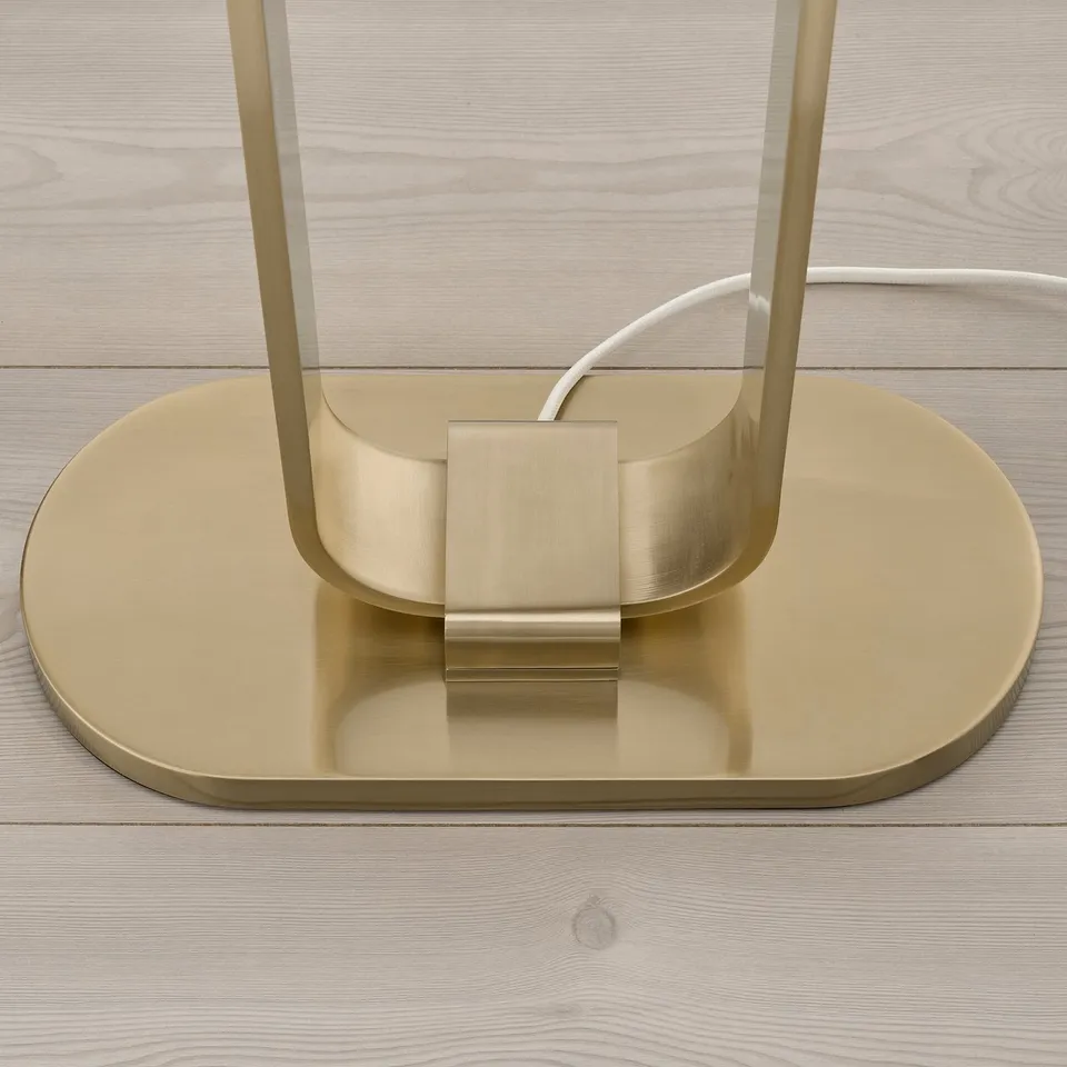 Modern gold-toned floor lamp base on light wooden floor. Glossy finish and sturdy design.