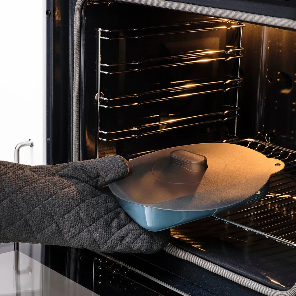Person placing dish with lid into oven. Lid is KLOCKREN silicone, multifunctional for oven and microwave.