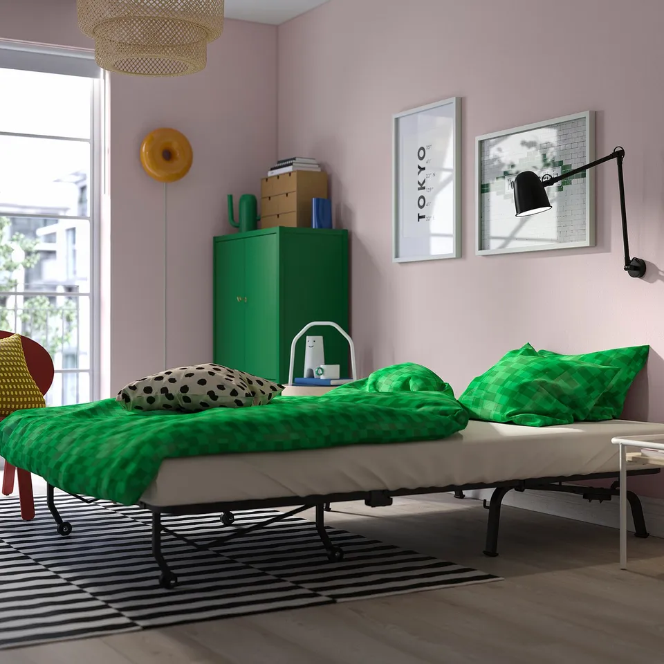 Modern guest room with convertible sofa-bed, vibrant green linens, art, and natural light.