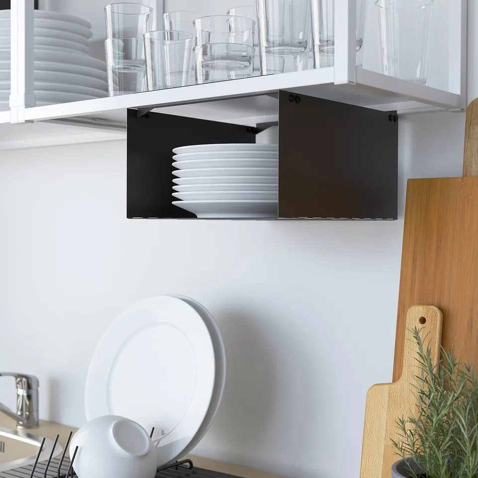 White kitchen shelves with glasses, plates, and stacked white plates on black shelf. Wooden boards against wall.