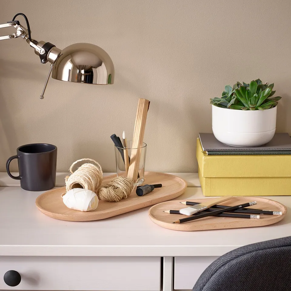 Wooden desktop with trays, mug, plant, pencils, and lamp.