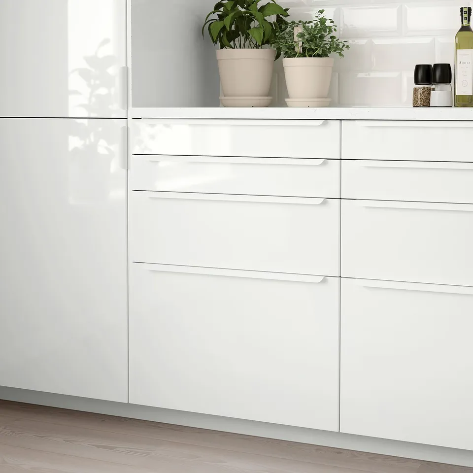 High gloss white RINGHULT kitchen drawer set, sleek and modern with smooth surfaces. House plants and seasonings on top, moderate in size.