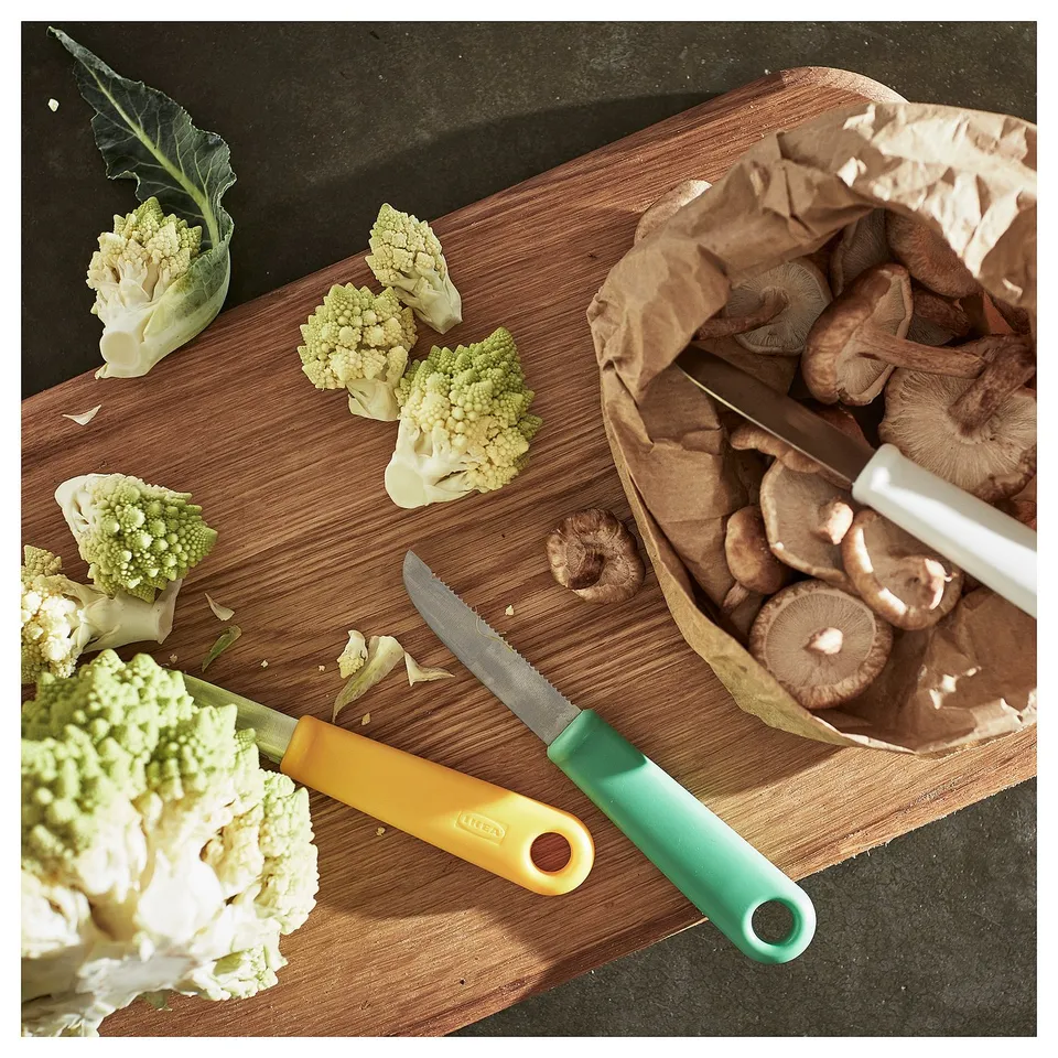 Two knives slicing veggies on wooden board.