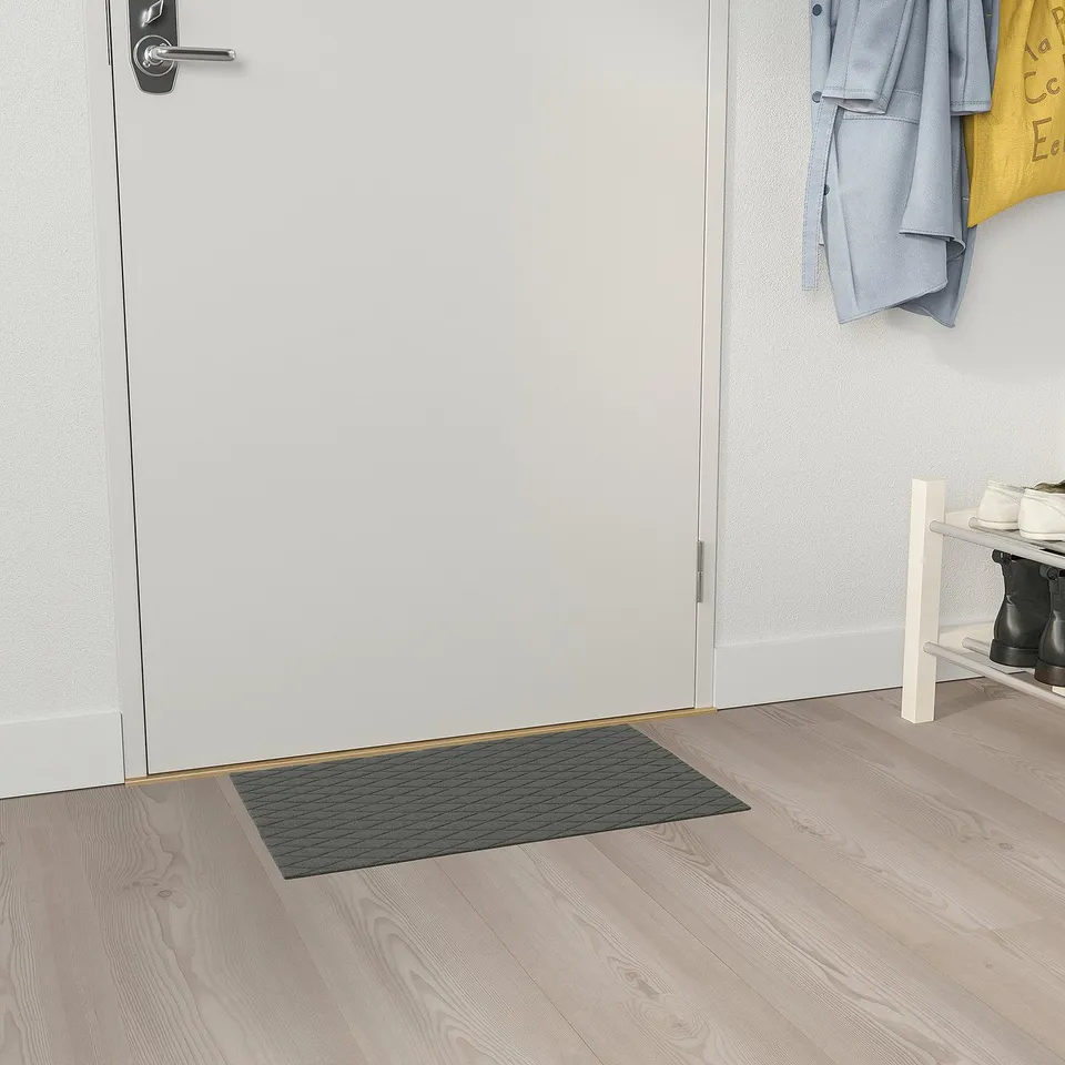 Entryway with white door, ÖSTERILD black mat, shoe rack, grey and yellow coats.