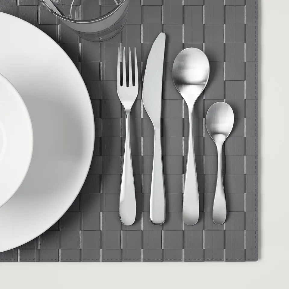 Silverware set on grey placemat: fork, knife, large and small spoons.