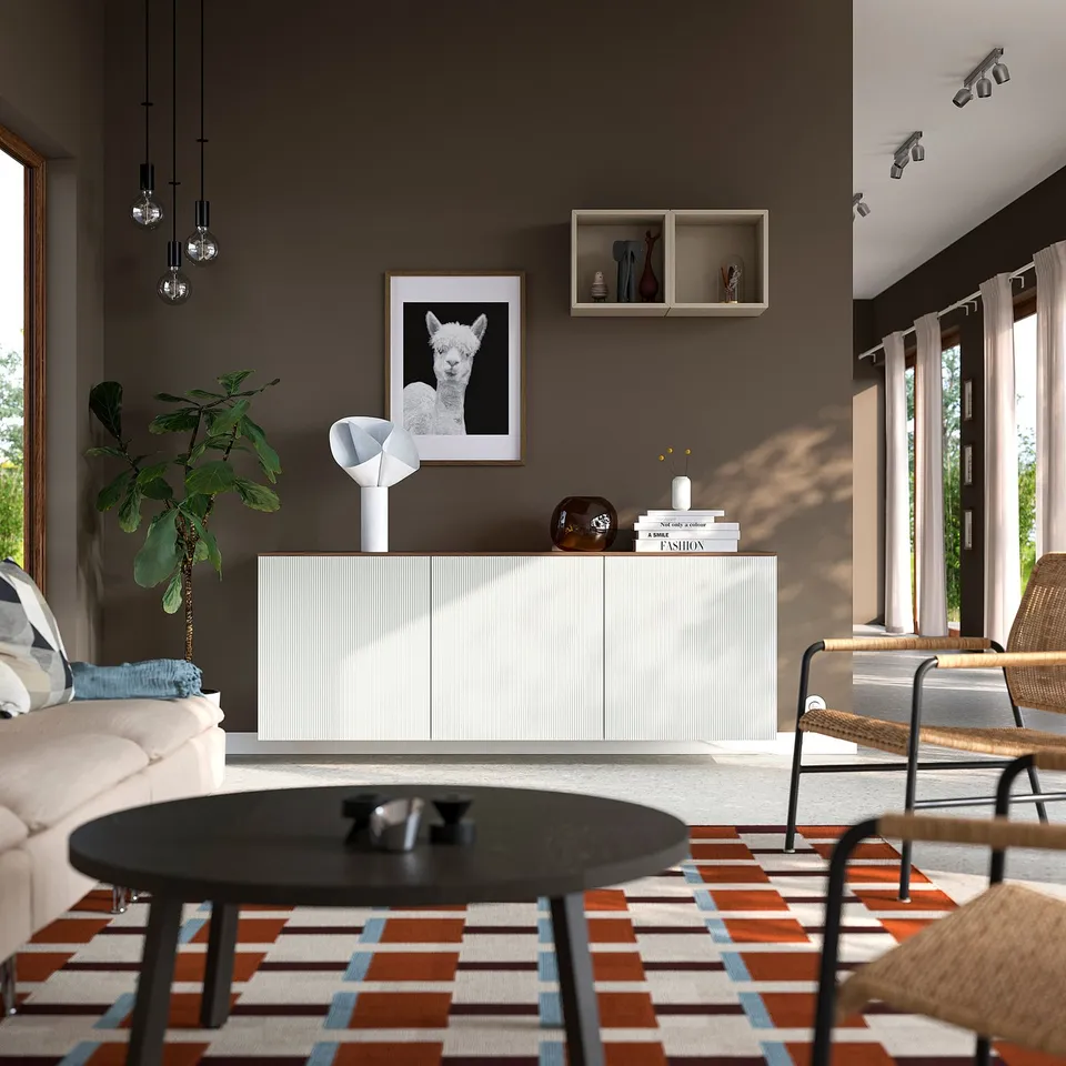 Modern living room with BESTÅ sideboard, lamp, vase, books, beige sofa, coffee table, rug, wicker chair, alpaca picture, and hanging lamps.