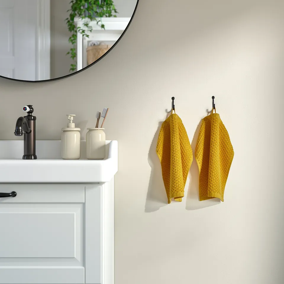 Modern bathroom with beige GULVIAL towels on hooks, enhancing decor with black sink fixtures and round mirror.