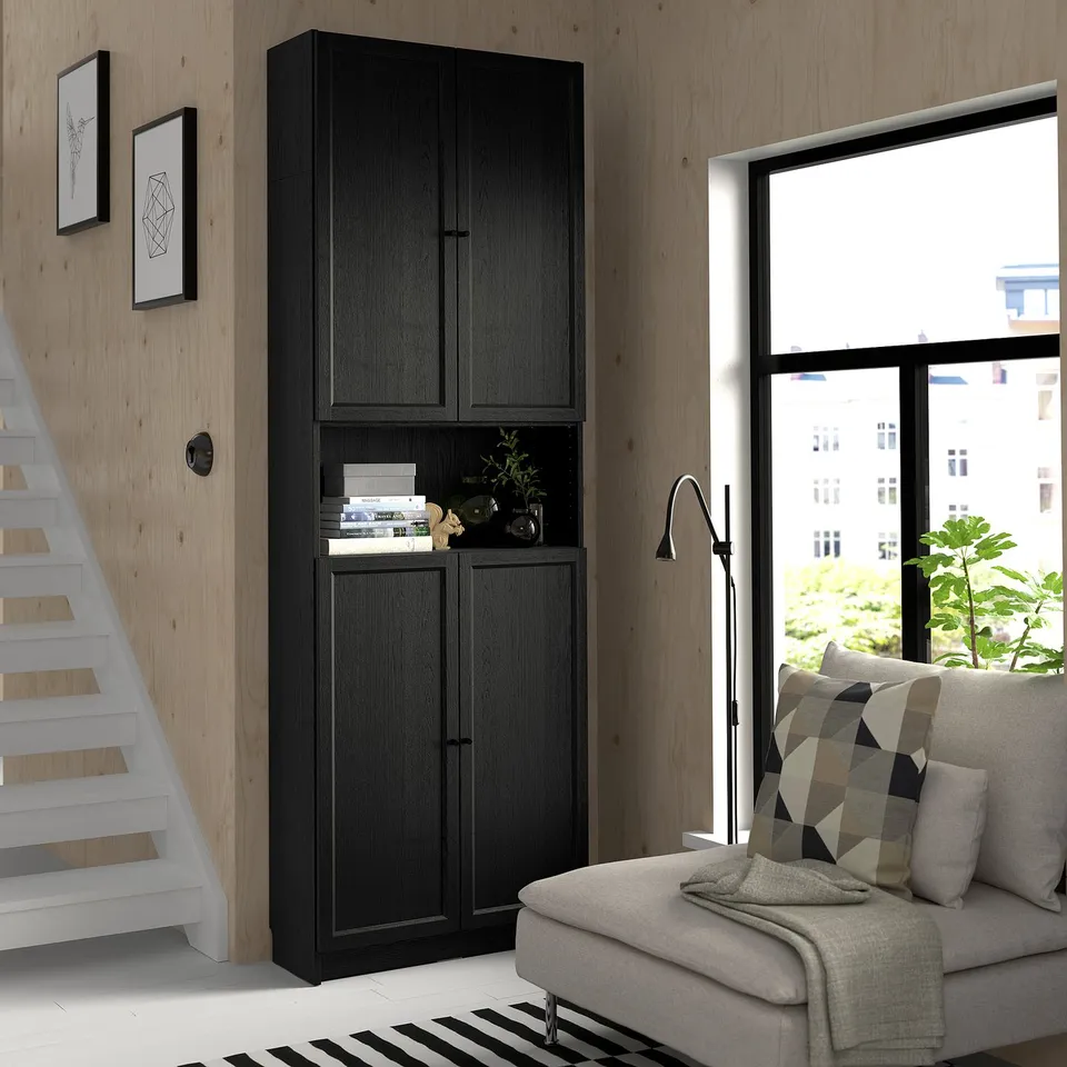 Modern living space with tall black BILLY bookcase next to stairs, grey sofa, large window, and black & white rug.