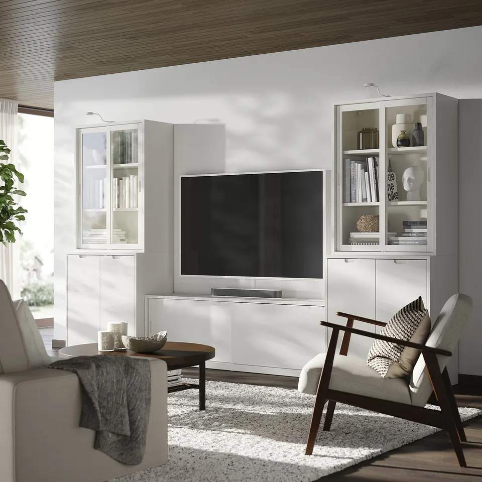 Modern minimalist living area with white TONSTAD tv unit, cabinets, and armchair. Wooden coffee table, soft rug, and decorative cushions.