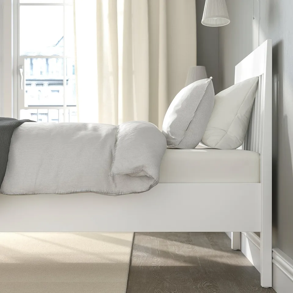 A modern bedroom with a white bed, pillows, and blankets. Natural light fills the room, creating a clean and cosy atmosphere.