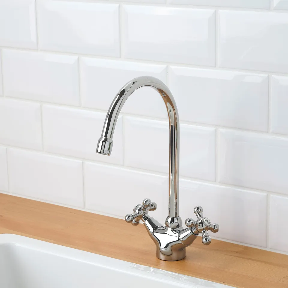 Chrome kitchen tap with two handles, set against white tiles, on a wooden countertop.