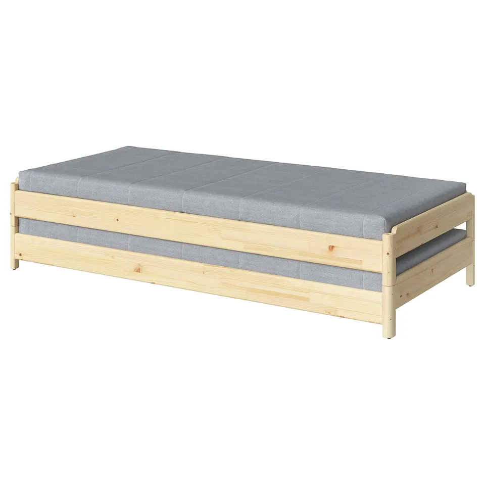 UTÅKER stackable wooden bed in natural colour, rectangular shape with grey cushions.