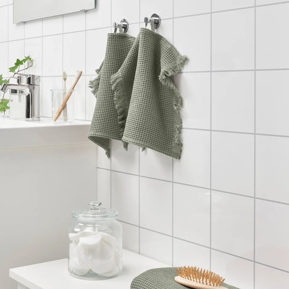 Green VALLASÅN towel above white sink with jar and brush.