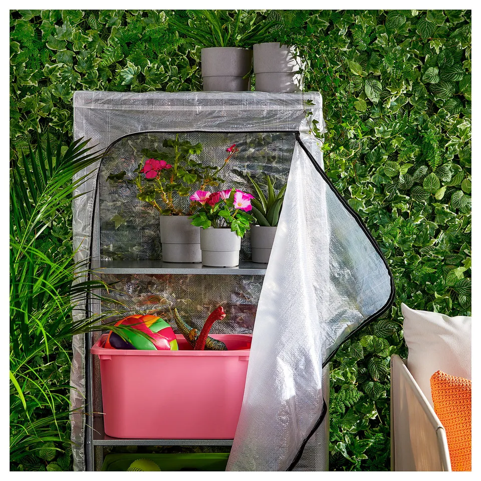Small greenhouse with pink tools, pink flowers, and grey pots on shelves. White cover and mesh sides.
