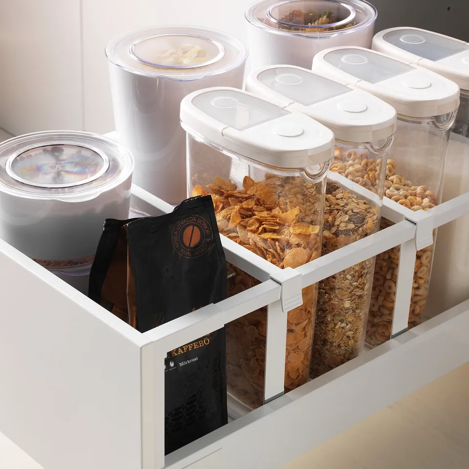 White kitchen drawer with adjustable shelves holding clear containers of cereal, nuts, and coffee bags.