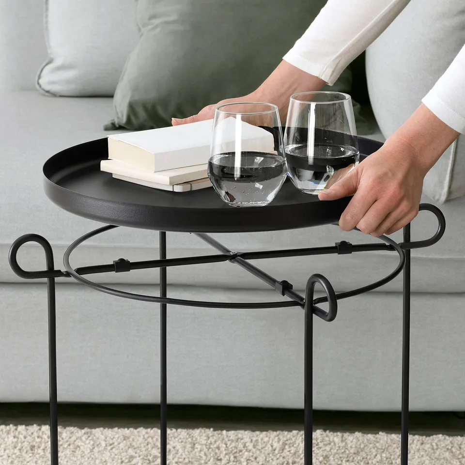 Person adjusting tray on LIVELYCKE side table with two glasses and a book, ideal for serving and storage.