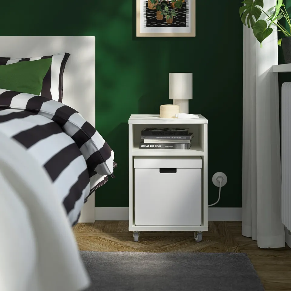 Green bedroom with white bedside table, books, lamp, black & white bed