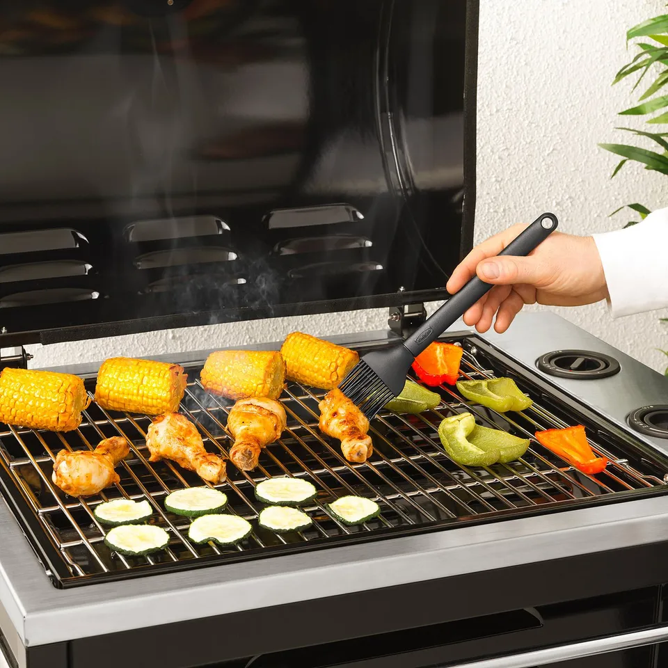 Person grilling various foods on a bbq grill using a silicone basting brush.
