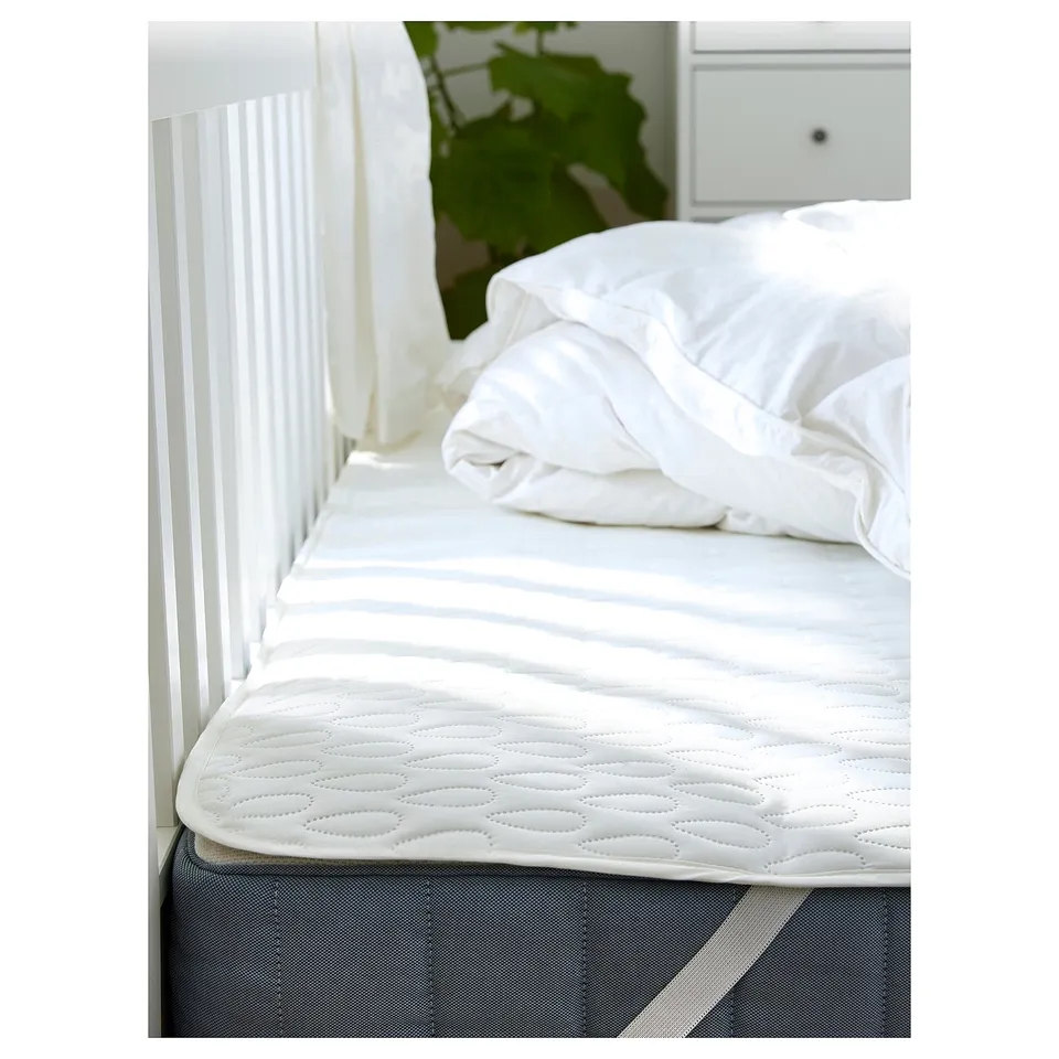A pristine white mattress topper with a quilted pattern on a grey base, neatly made on a bed with a white headboard and pillow.