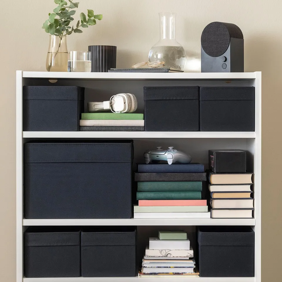 A white bookshelf with black fabric boxes and stacks of books.