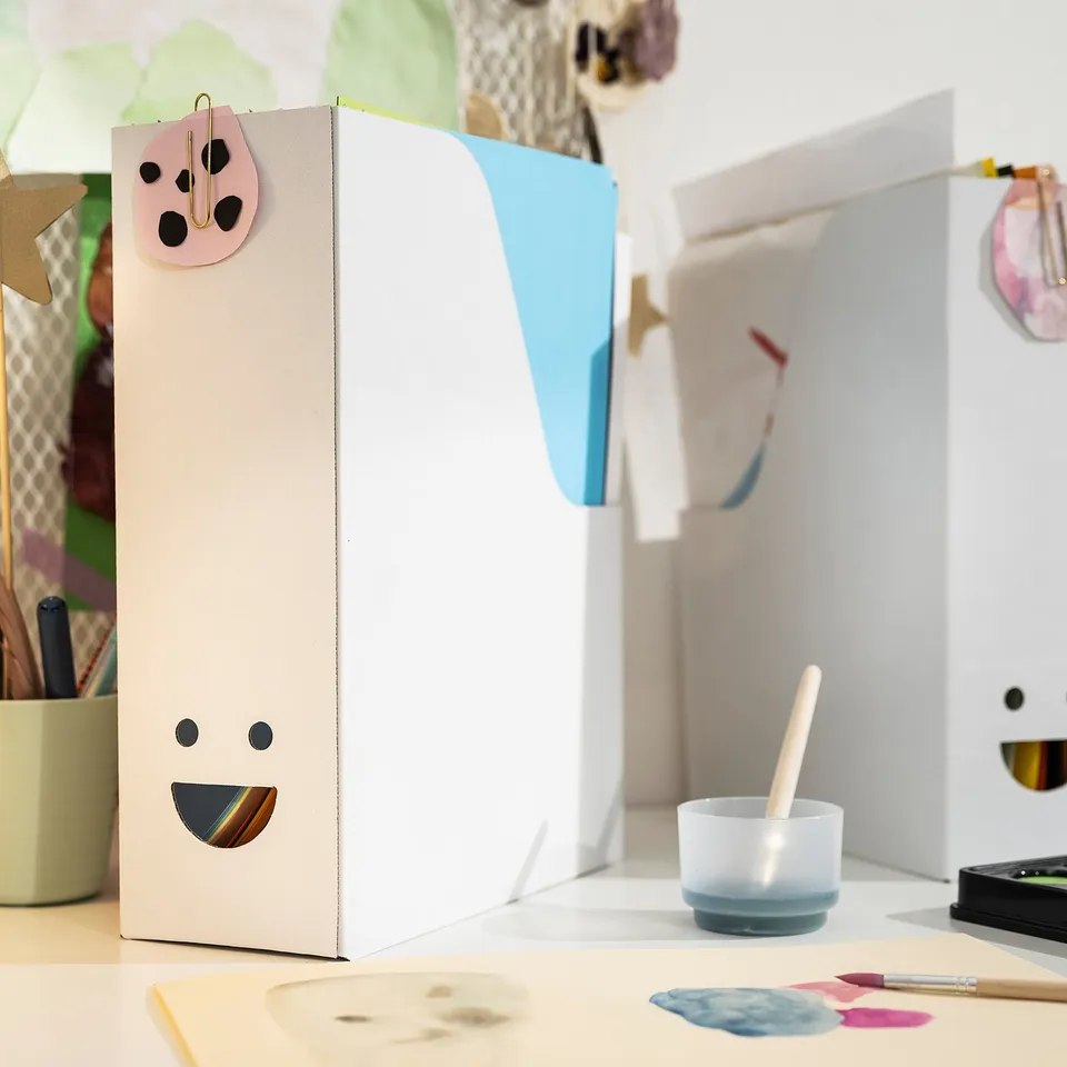 White TJABBA magazine file with smiley face, holding colourful papers.
