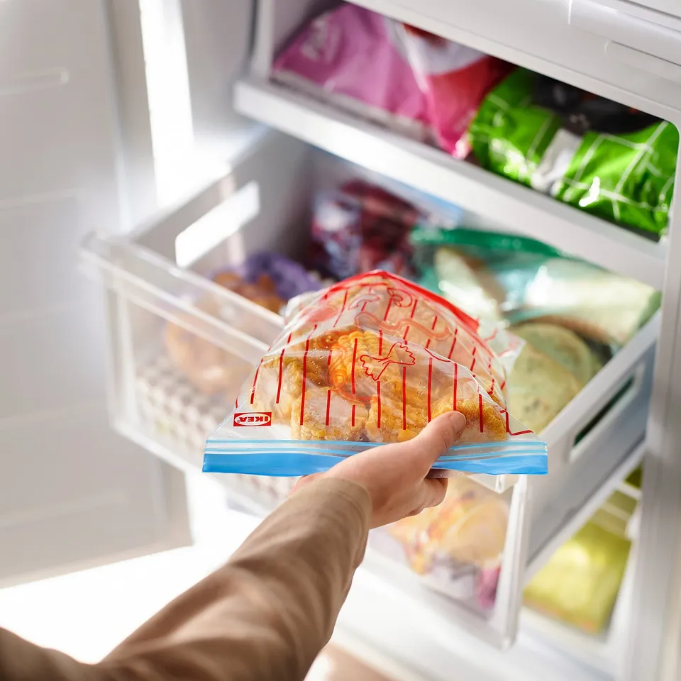 A hand holding a red and white food bag from an open refrigerator, showcasing its airtight, leakproof design.
