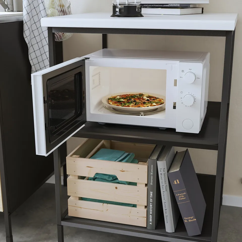 Small white microwave on shelf with pizza inside, next to books and storage boxes.