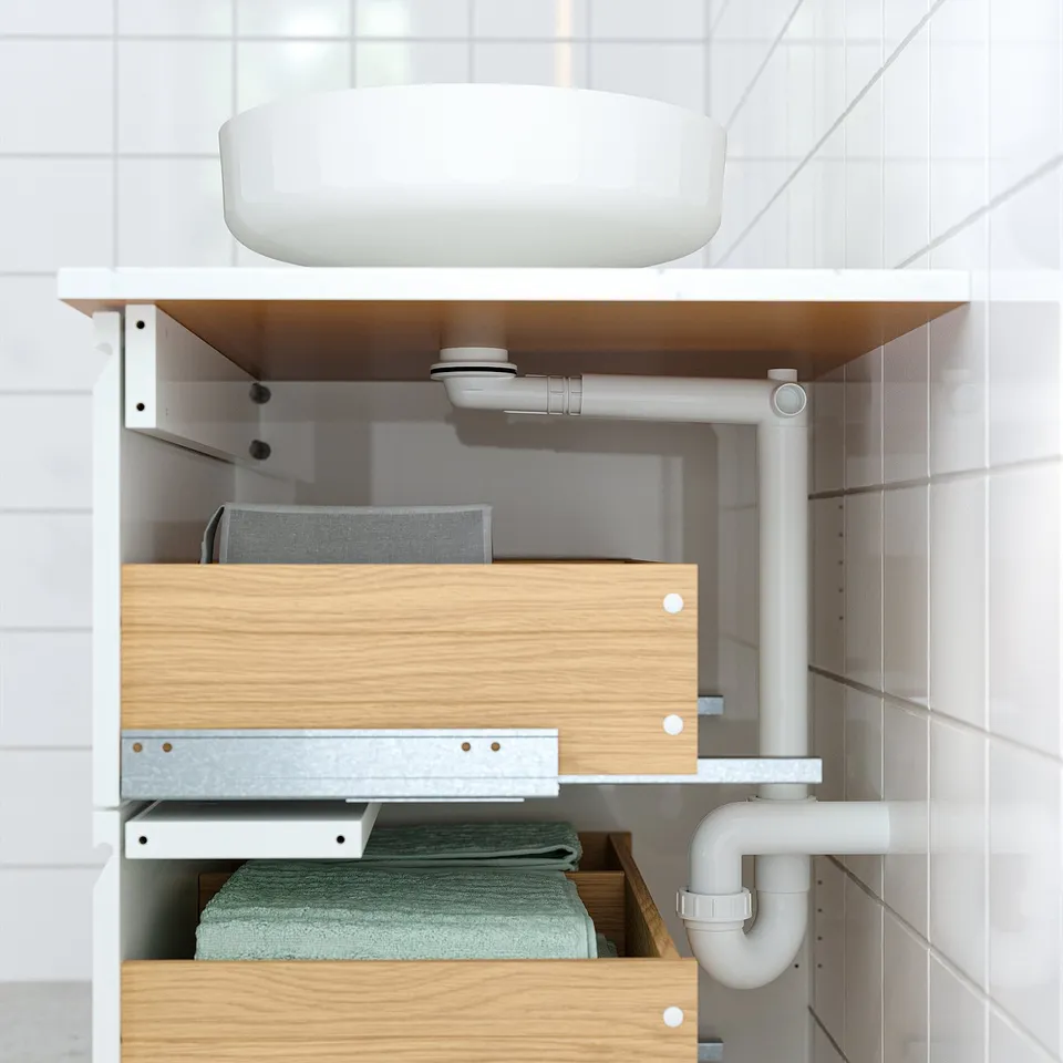Bathroom cabinet with drawers storing towels, pipes visible, secured for safety.