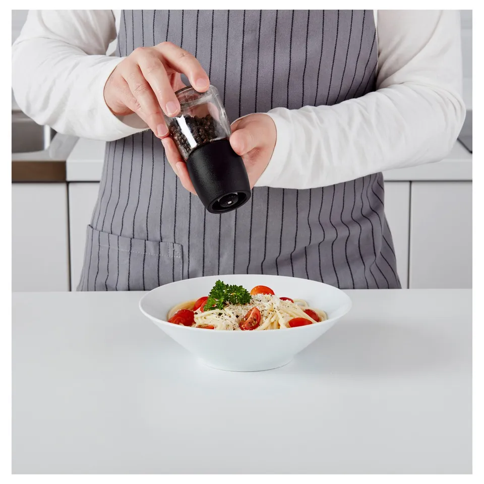 Person seasoning pasta with black pepper from IKEA grinder.