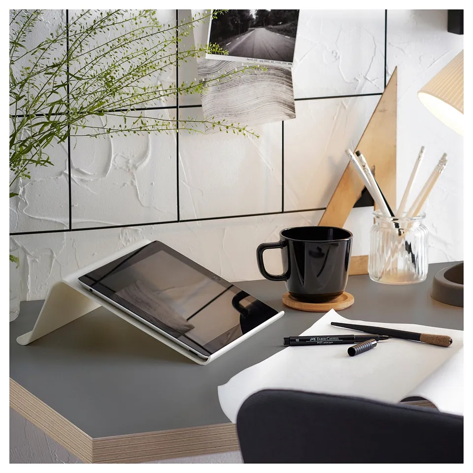 Modern workspace with tablet, black mug, pens, and plant on white desk.