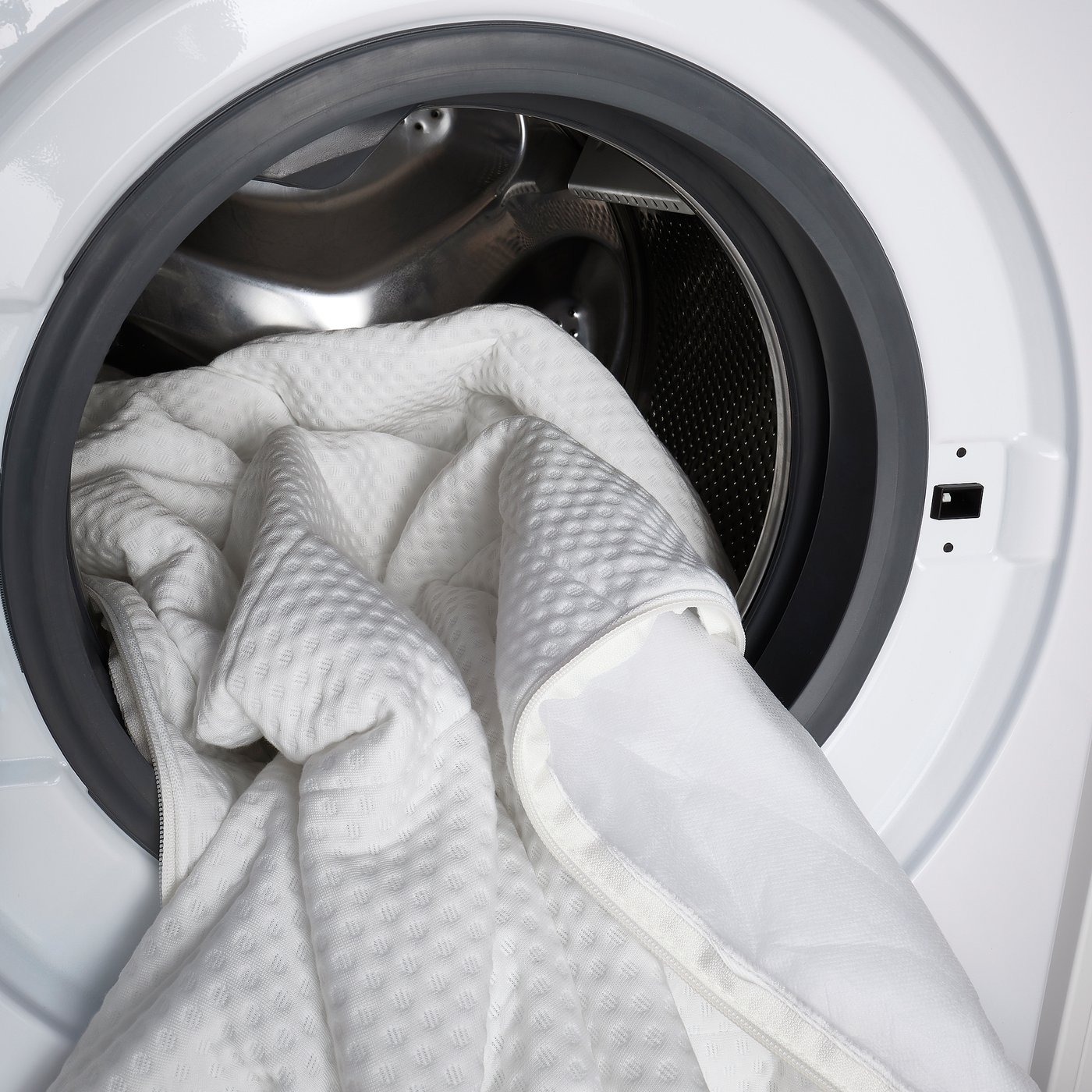 White washing machine filled with a rolled mattress, ready for cleaning.