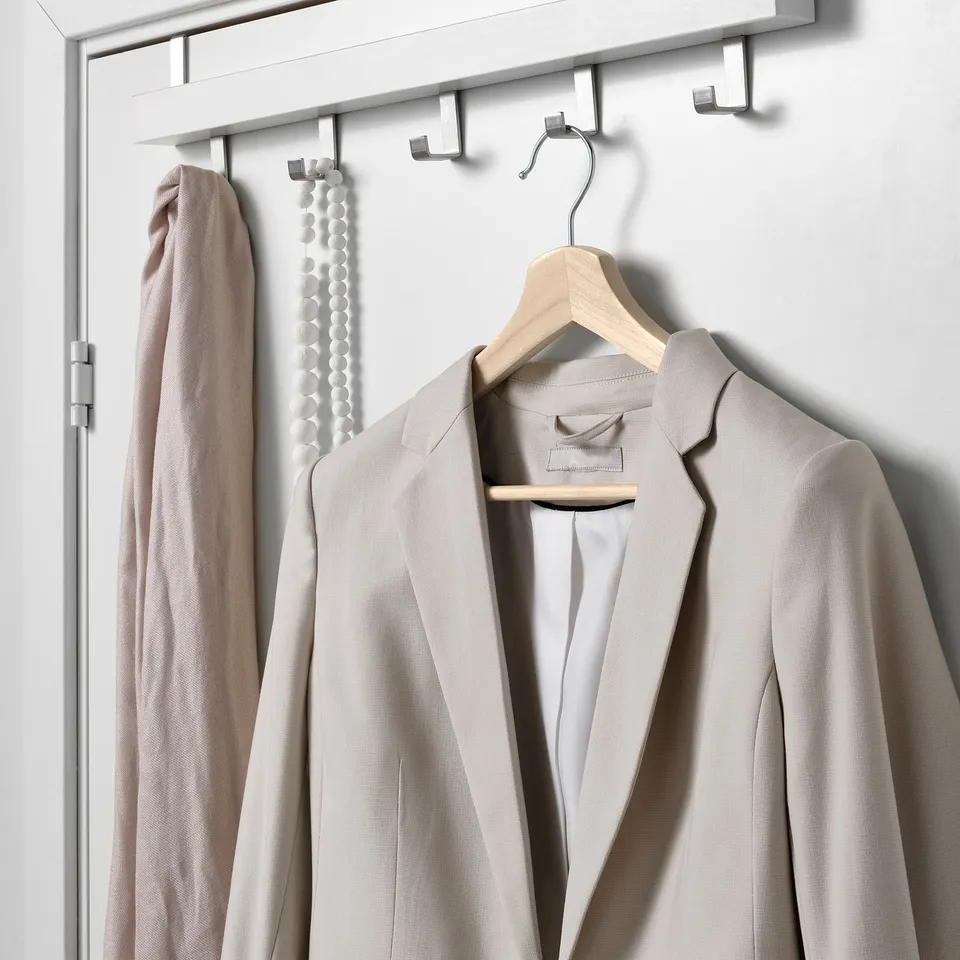 A beige jacket hangs on a wooden hanger, next to a light-colored scarf on a metal hook, showcasing an organised closet display.